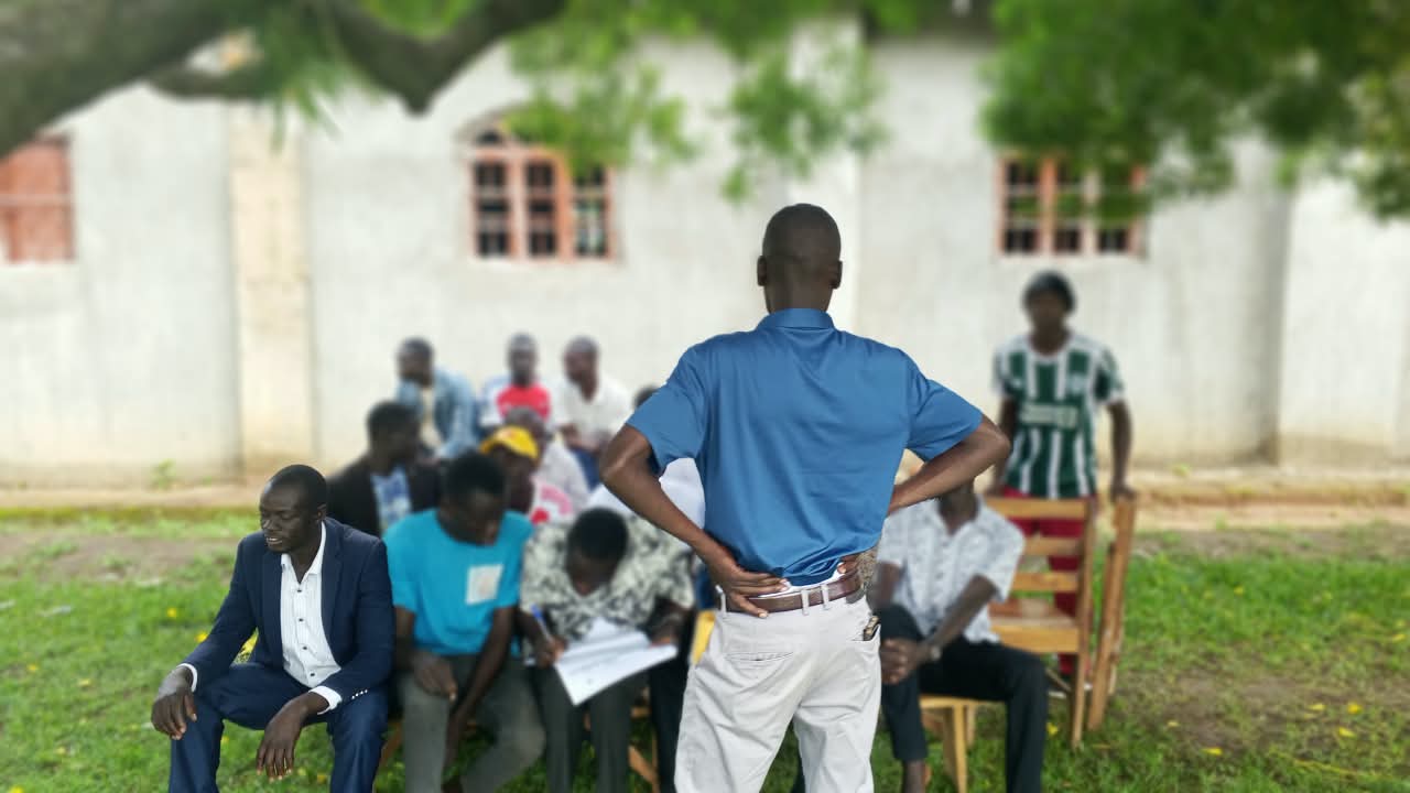 Facilitator addressing young men at an outdoor community session in Tororo District